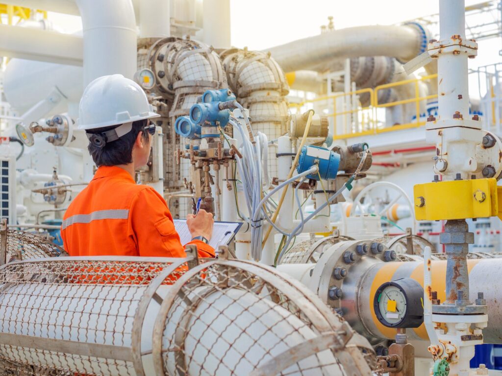 A technician studies the reading on a gas flow meter at an outdoor oil and gas facility
