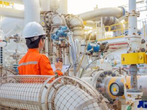 A technician studies the reading on a gas flow meter at an outdoor oil and gas facility