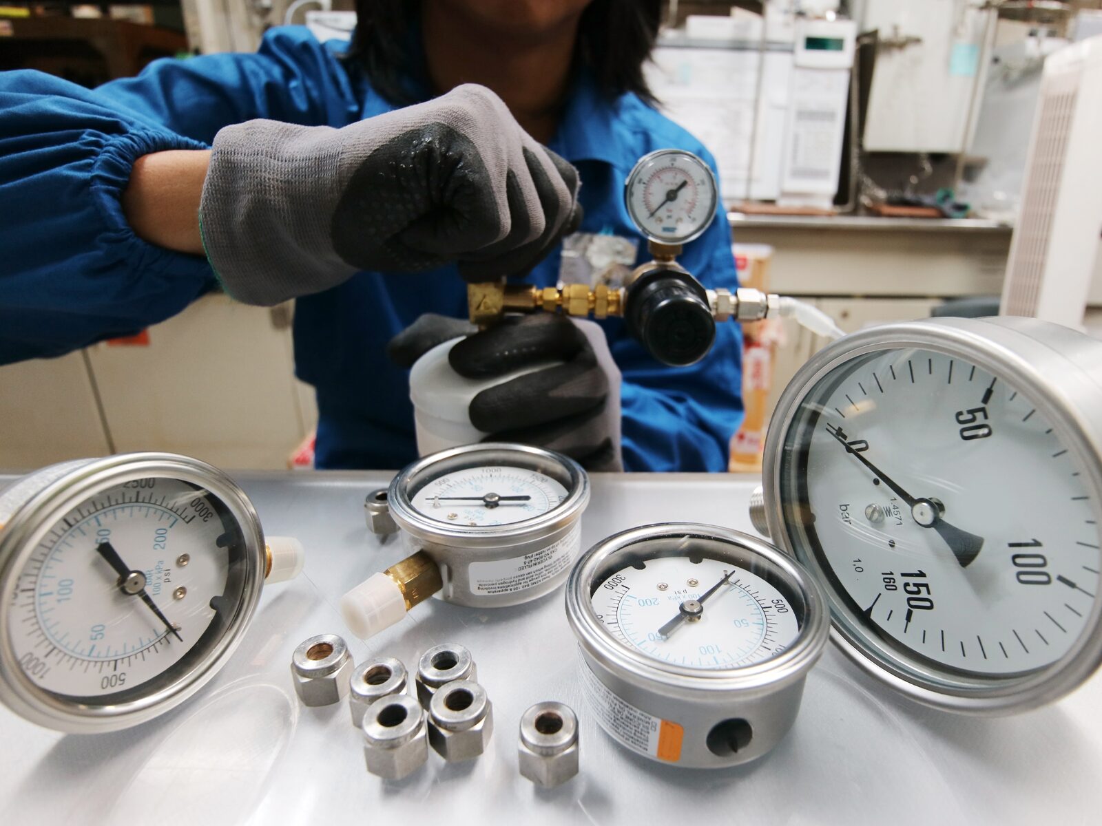 Technician calibrates a dial gauge. Several other gauges are on a table in the foreground.