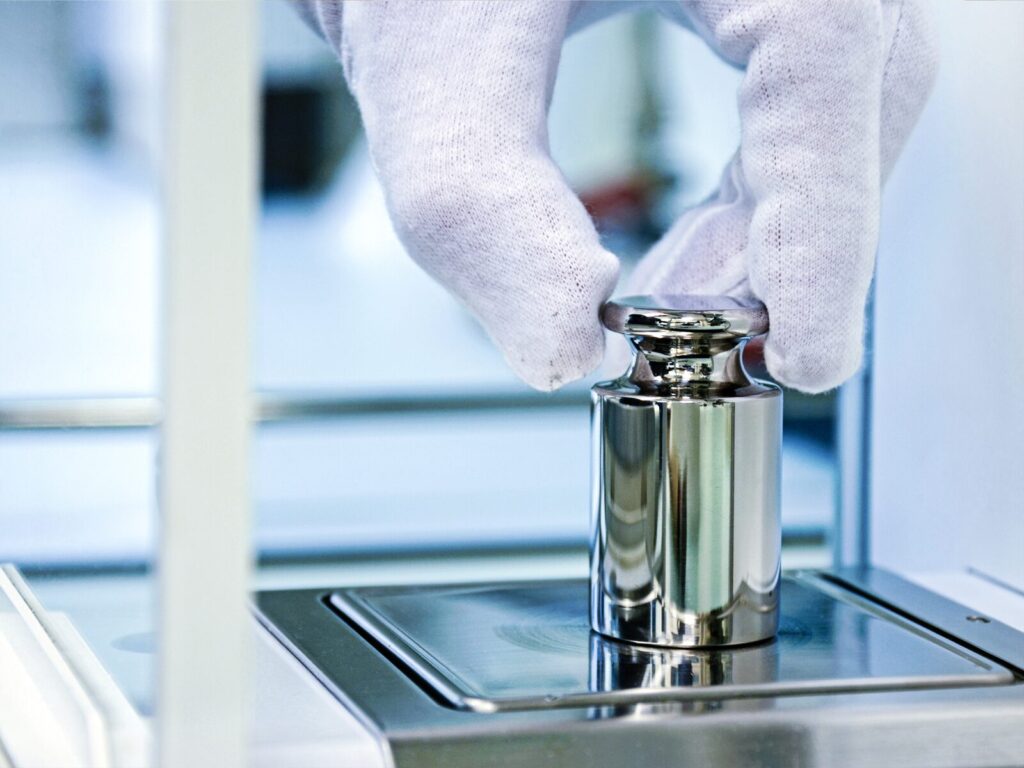A gloved hand places a calibration weight on a digital scale