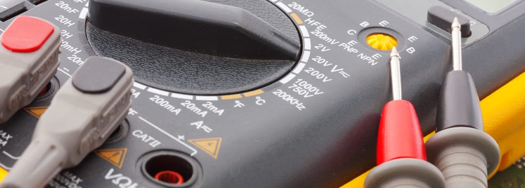 A yellow dial multimeter is connected to red and black terminals during a multimeter calibration service.