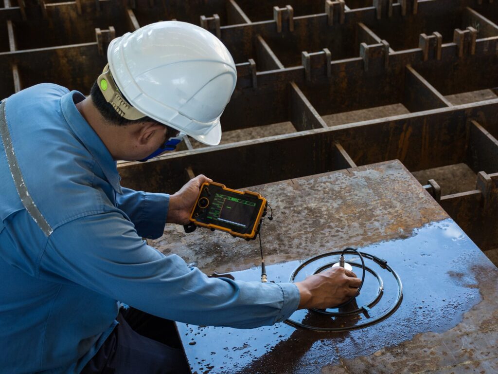 Technician uses an ultrasonic tester on a metal slab to identify the origin of a leak