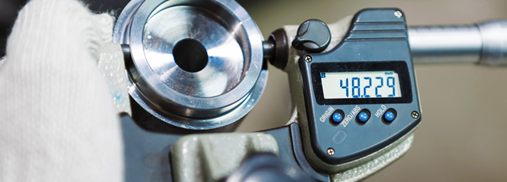 A digital snap gauge holds a circular automotive part in place for dimensional measurements.