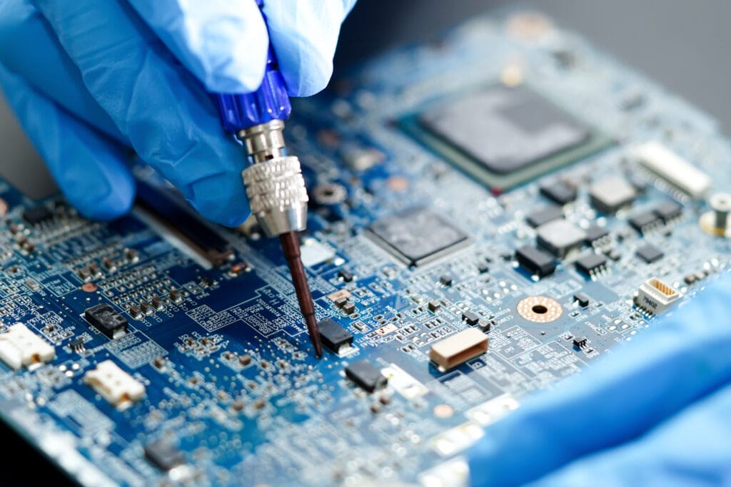 A blue circuit board under repair. A technician's gloved hands position a soldering iron over tiny circuit board components.