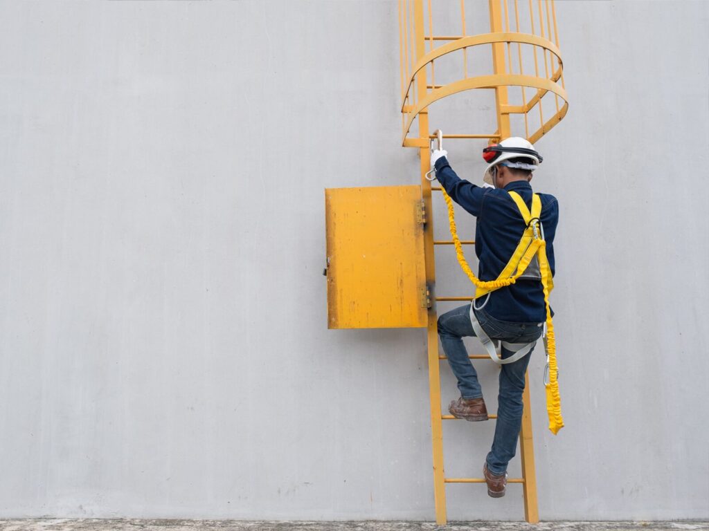 Rope access technician climbs a ladder. He wears a helmet and a protective harness.