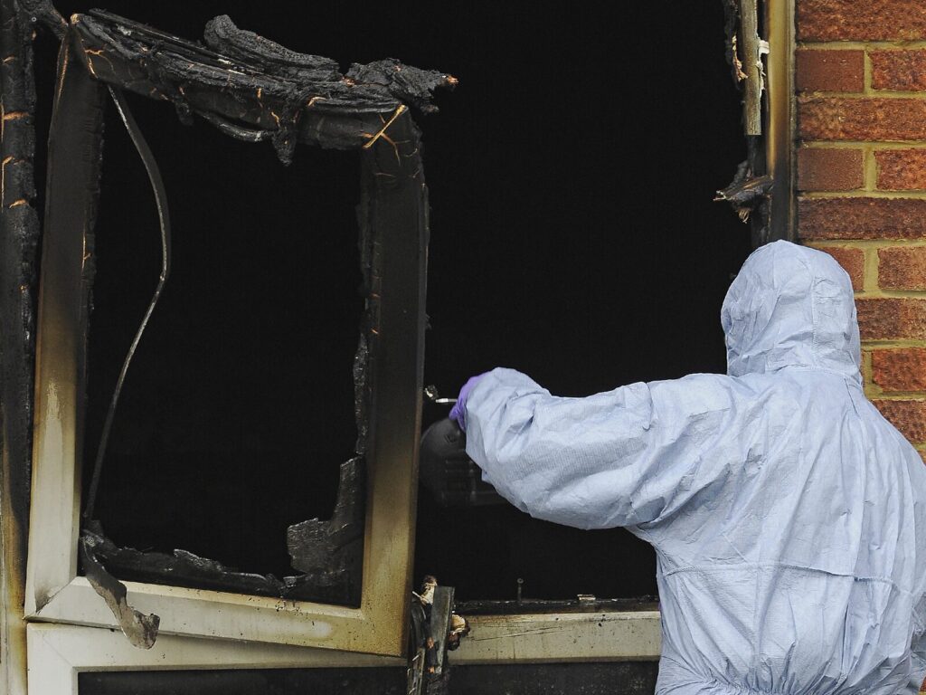 A certified fire investigator inspects a charred window frame in a burned building