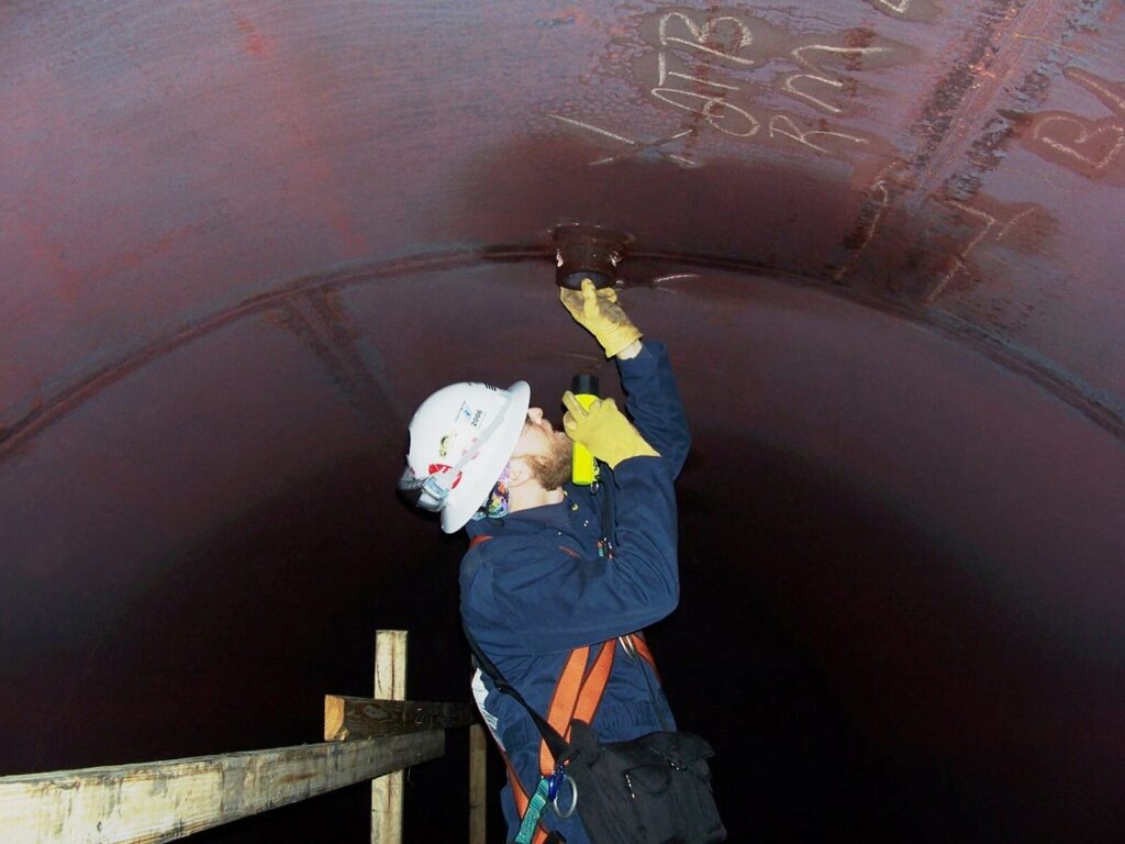 An engineer inspects a leak in a large industrial pipeline