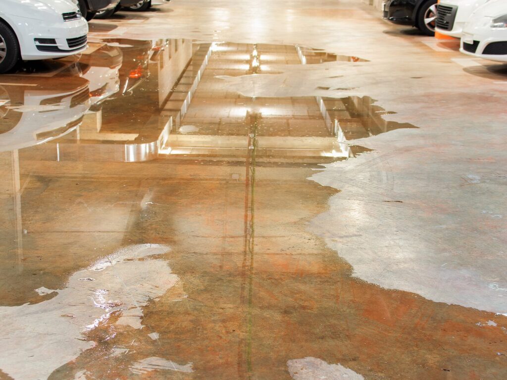 Parking garage with a massive water leak pooling around a row of cars