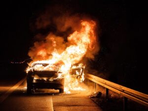 A car on fire on the side of the highway at night