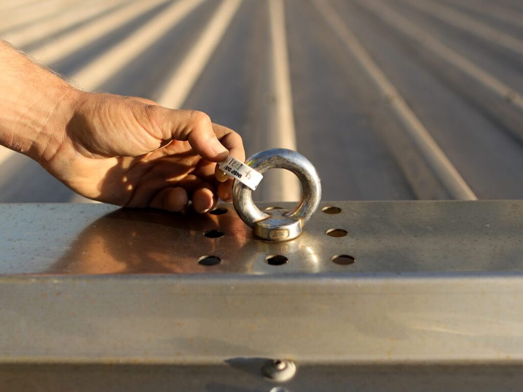 Technician holds out a certification tag for a roof anchor