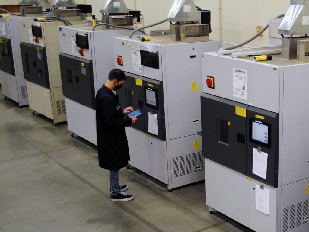 Expert stands in front of an ultraviolet testing chamber. He enters data into a tablet.