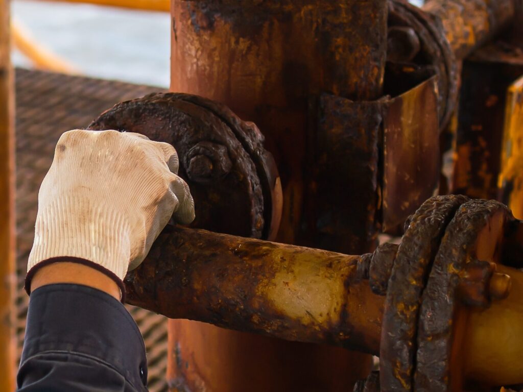 Expert's gloved hand touching a heavily corroded pipe installed in a pipeline.