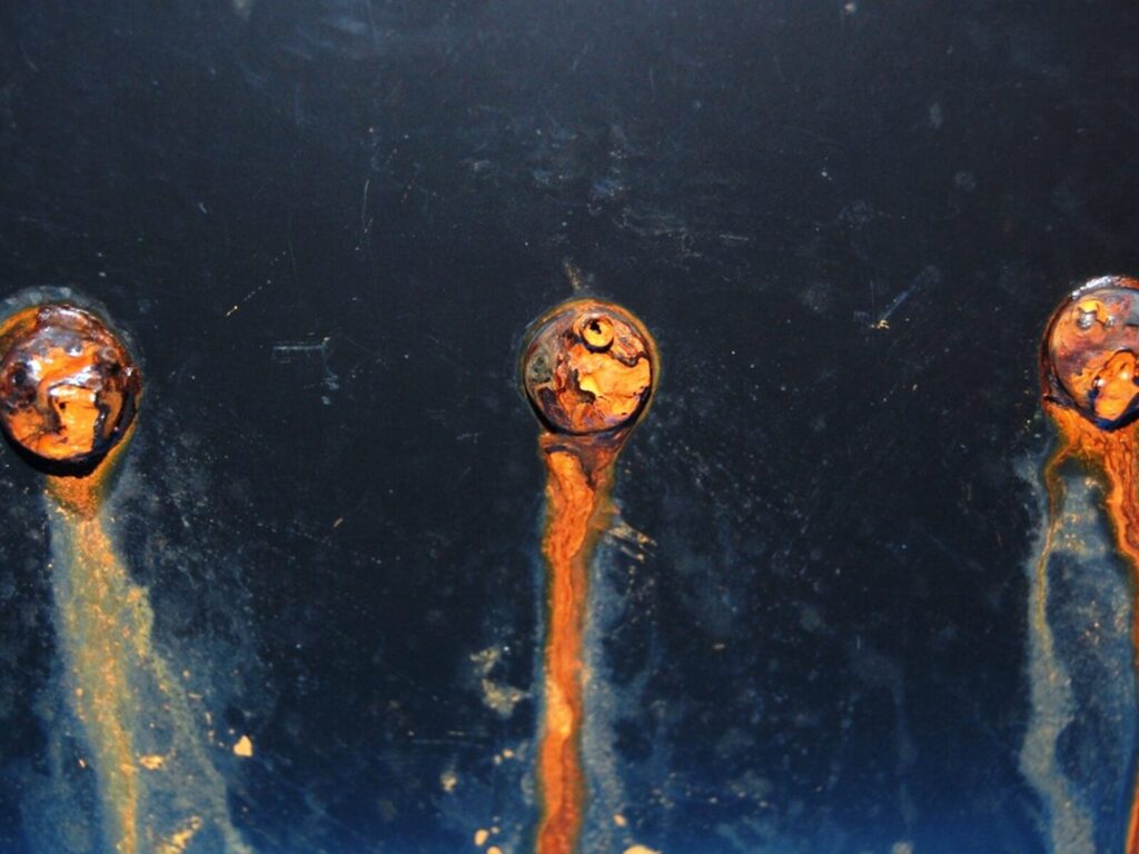 Heavily corroded nuts and bolts in a steel plate.