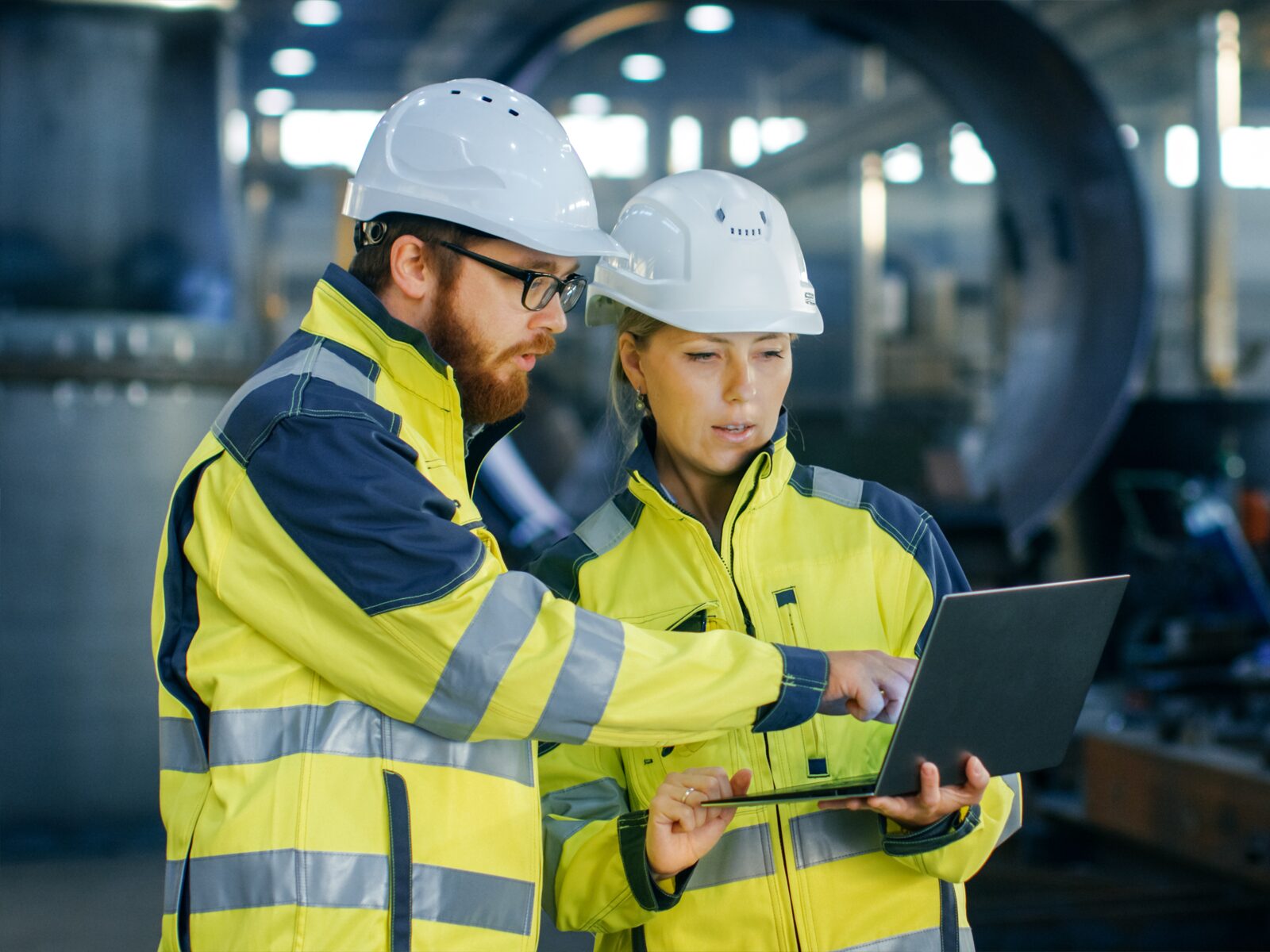 Two engineers study a laptop at an industrial facility