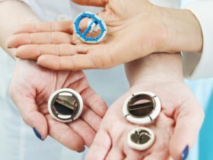 Three hands hold artificial heart valves of various colors