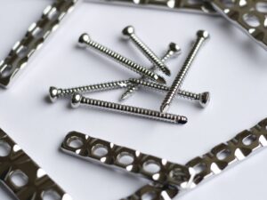 Metallic bone plates and screws for surgical implants