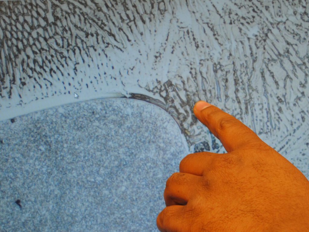 Technician points to a computer display of a microscopic defect in a weld