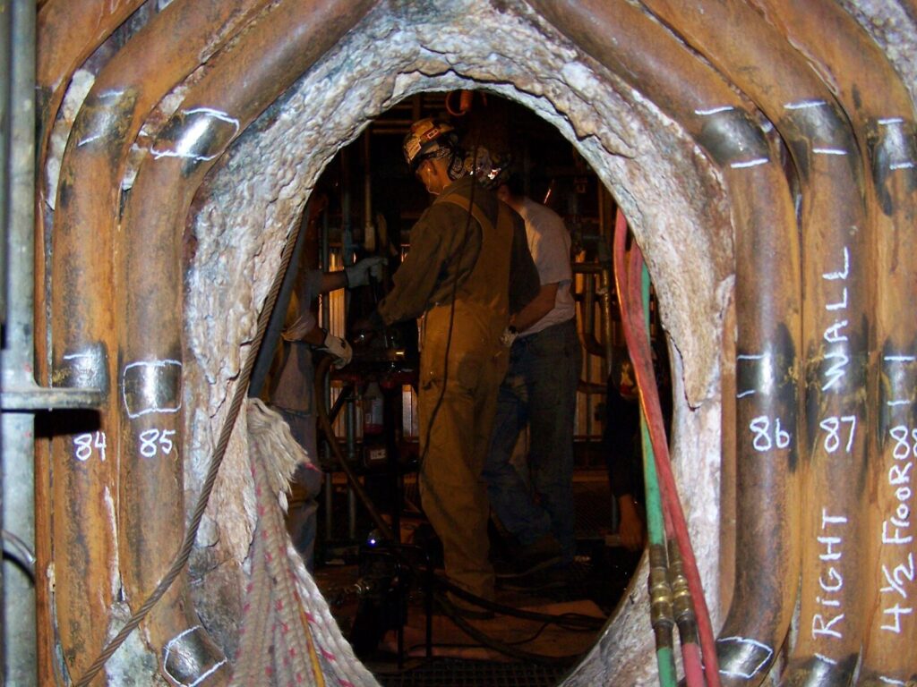 Three technicians framed by boiler tubes inside an industrial boiler.