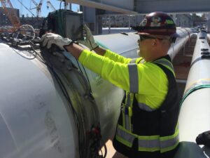 A nondestructive testing technician performs a phased array ultrasonic test on an above ground pipeline.