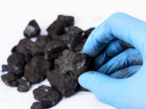 A scientist's gloved hand holds a sample of coal