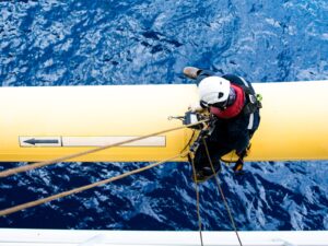 A rope access technician seated on a pipeline above water