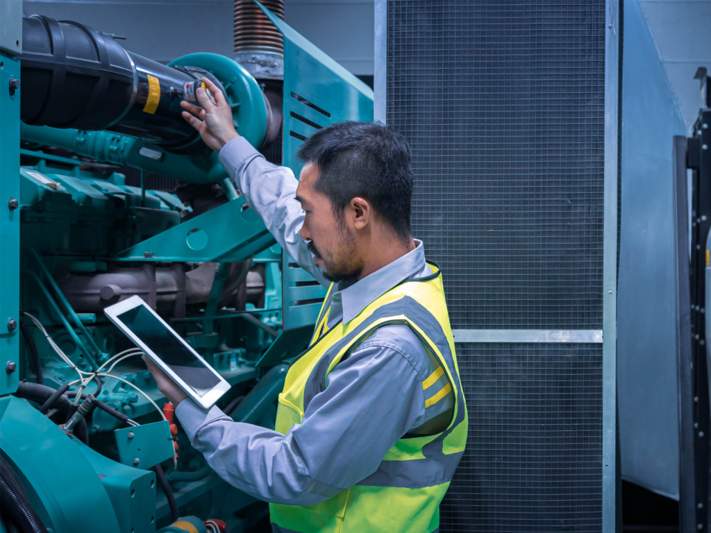 Engineer inspects a generator, logs data in his tablet