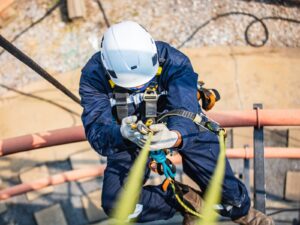 Worker scales the side of an industrial tank using fall protection and rope system