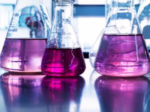 Three beakers of pink and purple liquid refract light onto the table below.