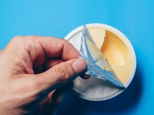 Hand peels the foil lid from a butter container