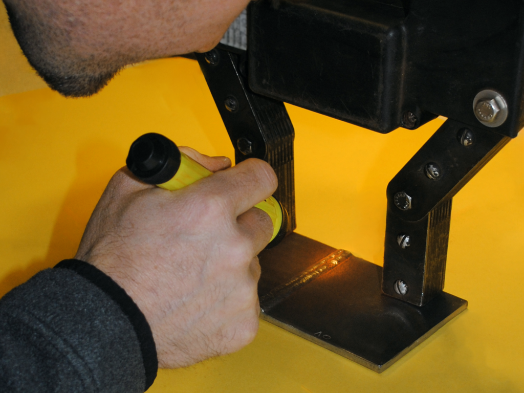 Technician shines a flashlight on a weld during magnetic particle testing.