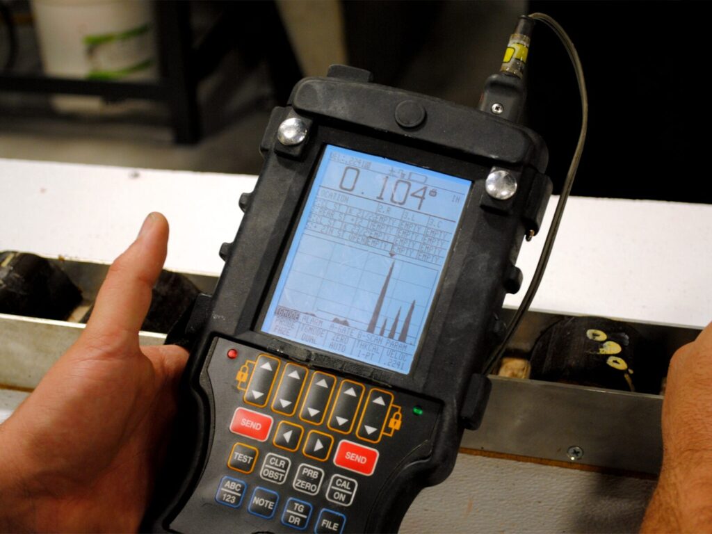 Technician holds an ultrasonic thickness tester over a metal flat bar
