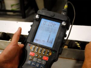 Technician holds an ultrasonic thickness tester over a metal flat bar