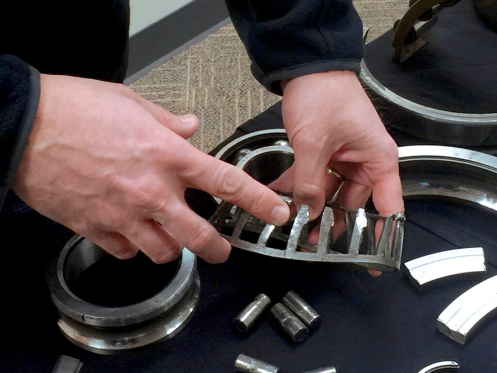 Technician holds a failed gear. He points to one of the teeth.