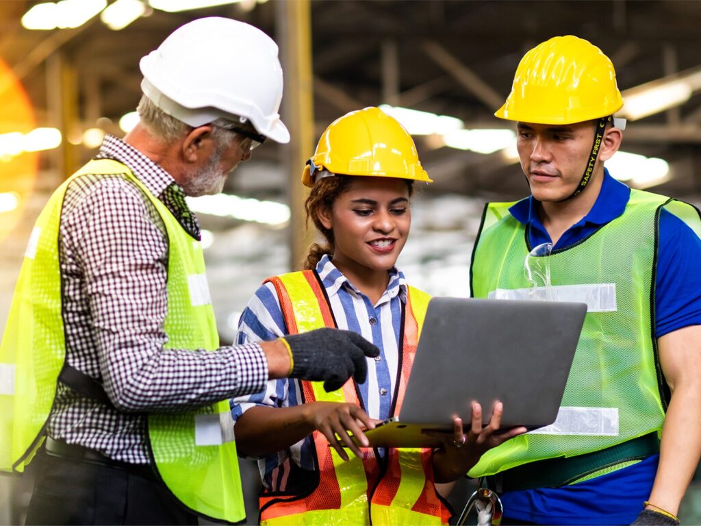 Three engineers gather around a laptop at a manufacturing plant