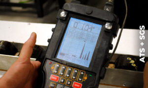 Technician holds an ultrasonic thickness tester over a metal flat bar