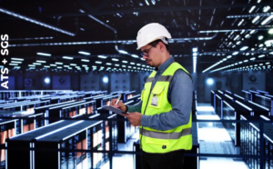 A technician in a yellow vest and hard had inspects a data center for quality assurance.